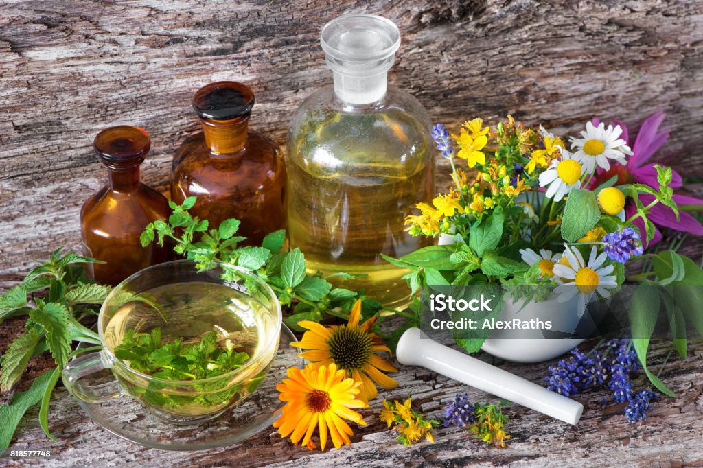 Cup of herbal tea with medicinal bottles and healing herbs in mortar Cup of herbal tea with tincture bottles and healing herbs in mortar on wooden table. Herbal medicine. Medicinal plants Alternative Medicine Stock Photo