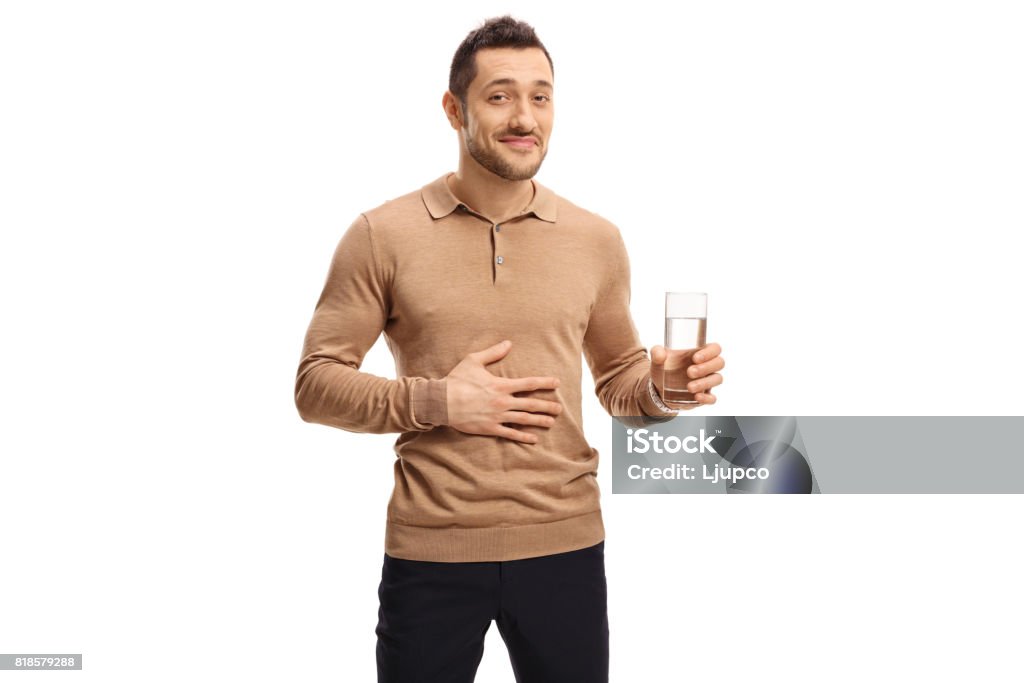 Young man with glass of water holding hand on stomach Young man with a glass of water holding his hand on his stomach isolated on white background Abdomen Stock Photo