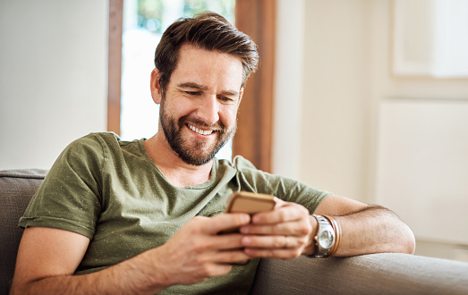 Shot of a happy young man using a mobile phone on the sofa at home