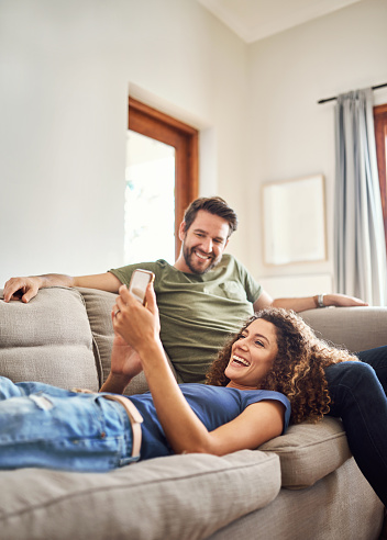 Shot of a happy young couple using a mobile phone together on the sofa at home