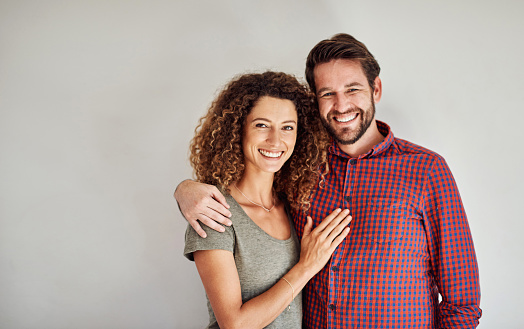 Portrait of a happy and loving young couple standing together against a gray wall