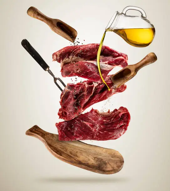 Flying pieces of raw steaks, with ingredients for cooking, served on woodenboard. Concept of food preparation in low gravity mode. Separated on smooth background. High resolution image