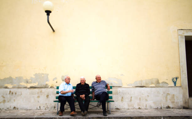 scicli, sicilia: tres hombres senior en banco; pared amarilla - scicli fotografías e imágenes de stock