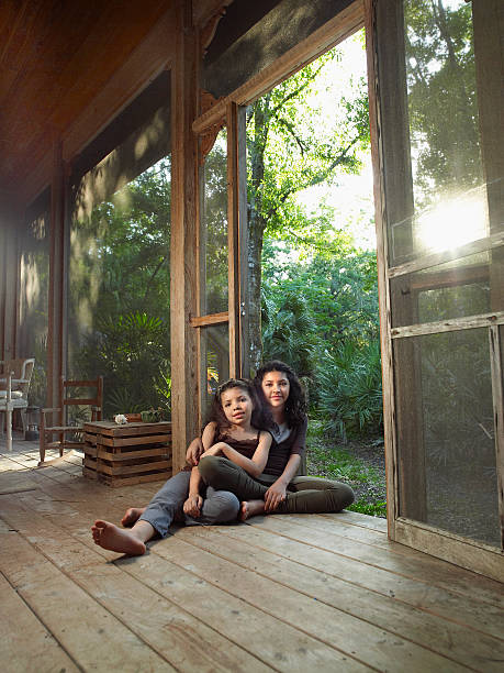 two mixed race young girls embrace each other sitting on screened porch - full length florida tropical climate residential structure - fotografias e filmes do acervo