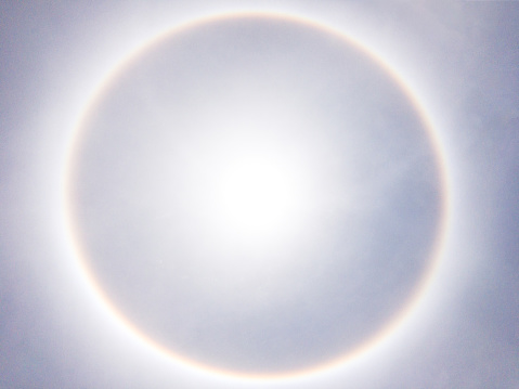 A halo  is an optical phenomenon produced by light (sun) interacting with ice crystals suspended in the atmosphere.