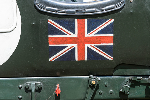 British Union Jack flag painted on the side of a vintage 1930 Bentley 4 1/2 Litre Supercharged English classic car in British racing green at a car show where people are looking at the cars. The car is on display during the 2016 Classic Days event at Schloss Dyck.