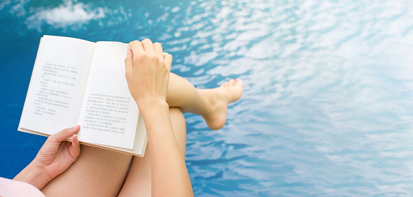Girl reading a book by the swimming pool. First person