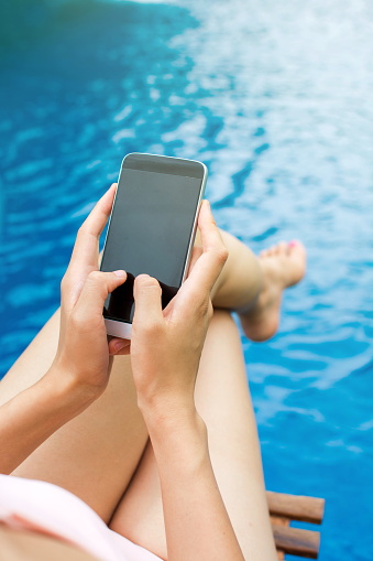 Girl using phone by the swimming pool, first person