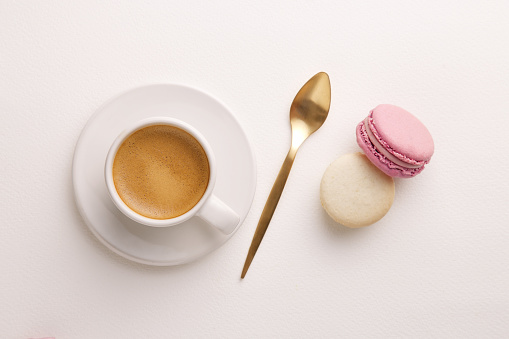 Coffee cup, macarons and golden spoon viewed from directly above. Colorful french dessert. White background. Top view