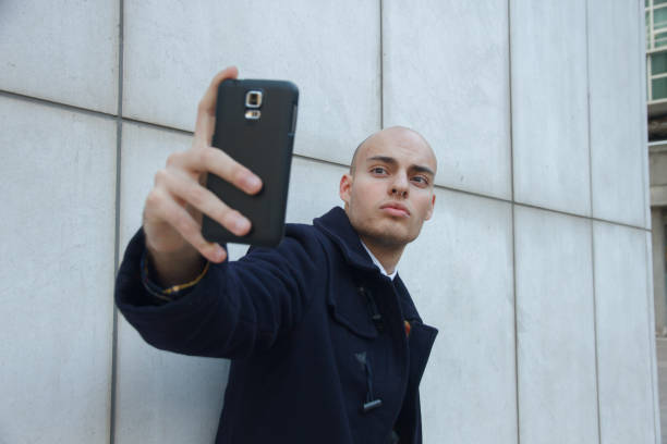 istock Young bald businessman holding a smart phone doing a selfie. 818869408