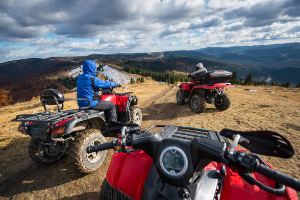 vista desde una cuatrimoto con hombres conducir un atv en frente en la parte superior la ruta de montaña con montañas de fondo perfecto, bosques y un cielo con nubes cúmulos en otoño - off road vehicle snow 4x4 driving fotografías e imágenes de stock