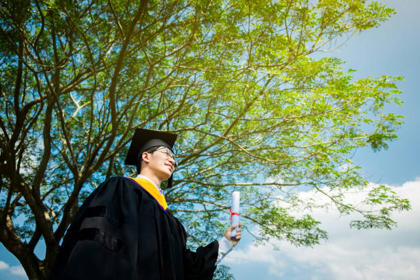 istock Graduation: Student standing up and smile holding Graduation certificate with Diploma With background in the nature. 818891938
