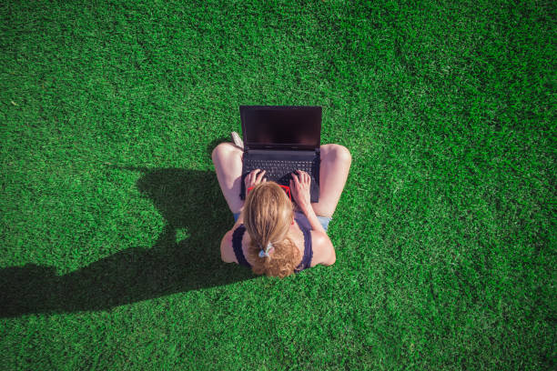istock Young female sitting on grass and using blank screen laptop 818896852