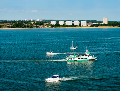 People aboard a small passenger ferry and a variety of leisure craft in the calm waters of Southampton Water in Hampshire, England, on a hot summer day.