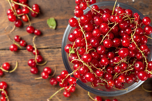 Red currant in a glass plate and scattered next to a plate on a brown wooden background\