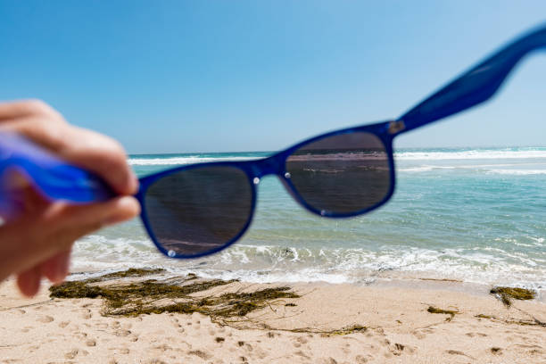 istock POV hand holding sunglasses at the beach. 819031242