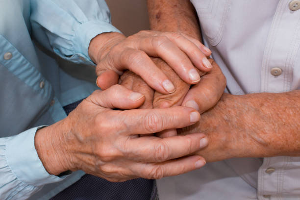 istock Hands of two loving senior people on a dark background 819129930