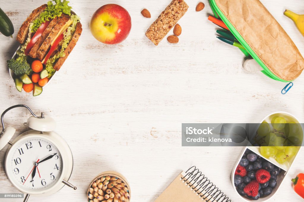 Sandwich, apple, grape, carrot, berry in plastic lunch boxes, stationery and bottle of water Sandwich, apple, grape, carrot, berry in plastic lunch boxes, stationery and bottle of water on white background. Back to school concept. Learning Stock Photo