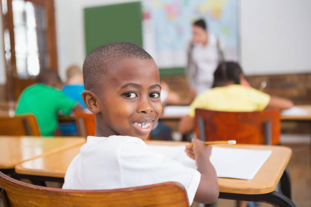 istock Cute pupil smiling at camera at his desk in classroom 819187730