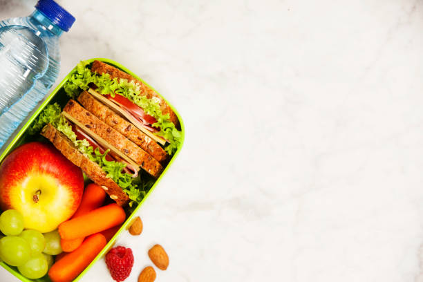 Green school lunch box with sandwich, apple, grape, carrot and bottle of water stock photo