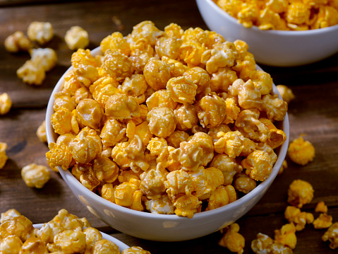 Tasty cheese popcorn falling out of a blue striped carton bucket, isolated on white background. Scattering of popcorn grains. Movies, cinema  and entertainment concept.