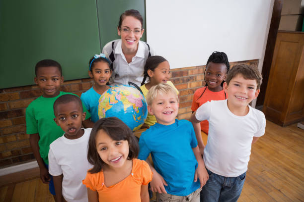 istock Cute pupils smiling around a globe in classroom with teacher 819229170