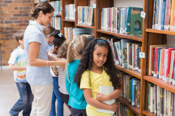 istock Cute pupils and teacher looking for books in library 819234810