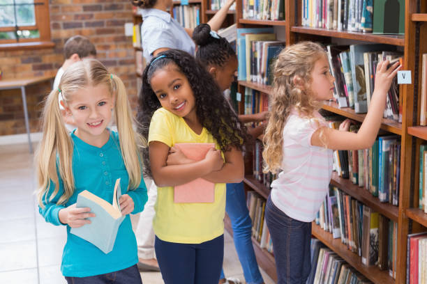 istock Cute pupils and teacher looking for books in library 819283592