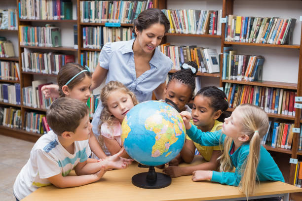 istock Cute pupils and teacher looking at globe in library 819287774