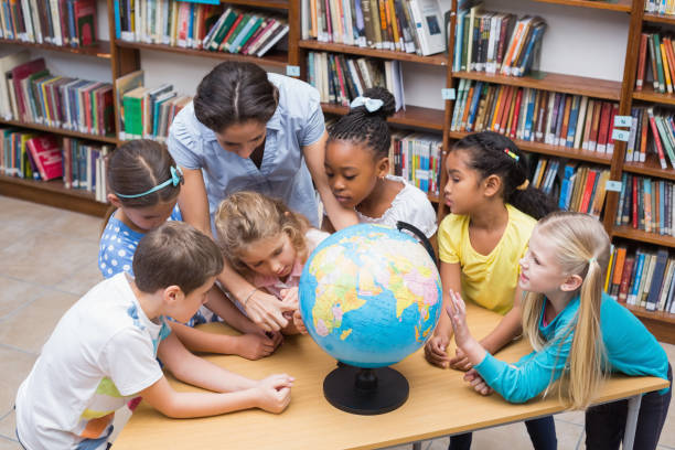 istock Cute pupils and teacher looking at globe in library 819287808