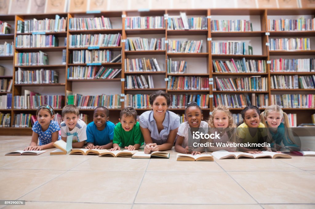 Bonitos alunos e professor, deitado no chão na biblioteca - Foto de stock de 30 Anos royalty-free