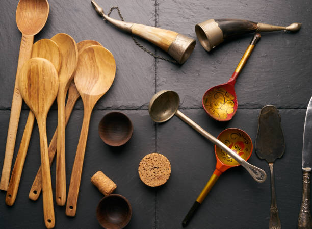 istock Various kitchen utensils wooden spoon round cutting board bower silver knife and spatula wooden bowls for sauce horn for wine on black stone background. 819303124