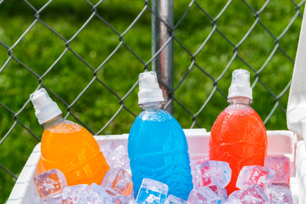 Cooler full of Ice cold colorful sports drinks A red and white ice chest full of ice and several plastic bottles of colorful ice cold sports drinks on a hot Summer day with a chain link fence in the background. energy drink photos stock pictures, royalty-free photos & images