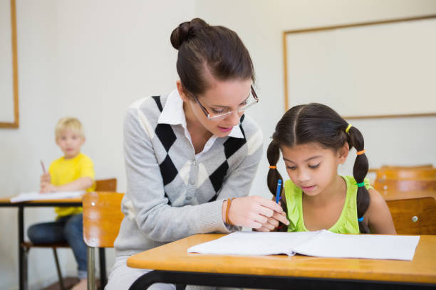istock Pretty teacher helping pupil in classroom 819382356