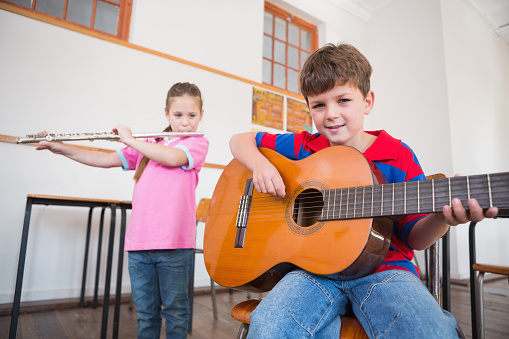 Cute pupils playing flute and guitar in classroom at the elementary school