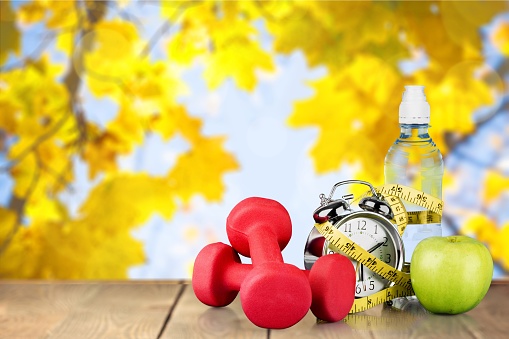 Dumbbells with measuring tape and apple for diet concept on autumn background