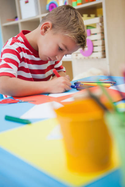 istock Cute little boy cutting paper shapes in classroom 819424778