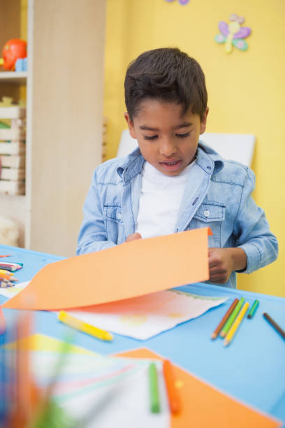 istock Cute little boy cutting paper shapes in classroom 819424804