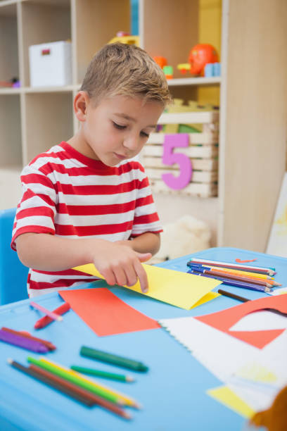 istock Cute little boy folding paper shapes in classroom 819424864