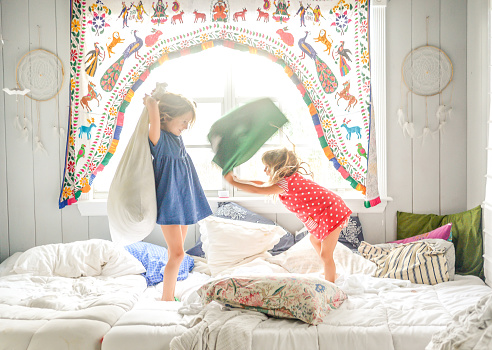 Two little girls, kids in a candid shot having a pillow fight in bed