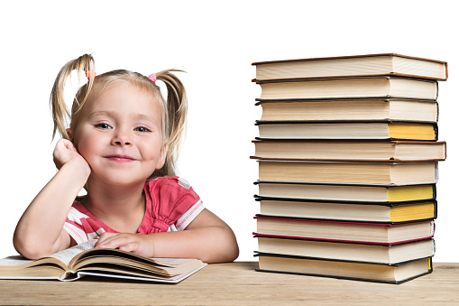 Portrait of a beautiful smiling little girl sitting at a desk with a stack of books isolated on a white background