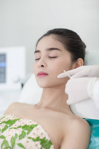 Face Care. Facial Laser Hair Removal. Beautician Giving Laser Epilation Treatment To Young Woman's Face At Beauty Clinic; Hairless Smooth And Soft Skin;  Asian girl;  Health And Beauty Concept. stock photo