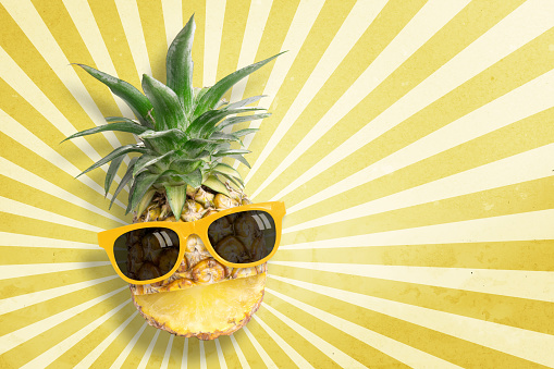 Pineapple wearing sunglasses on sunbeam vintage background with copy space and pastel tone. In summer holiday.