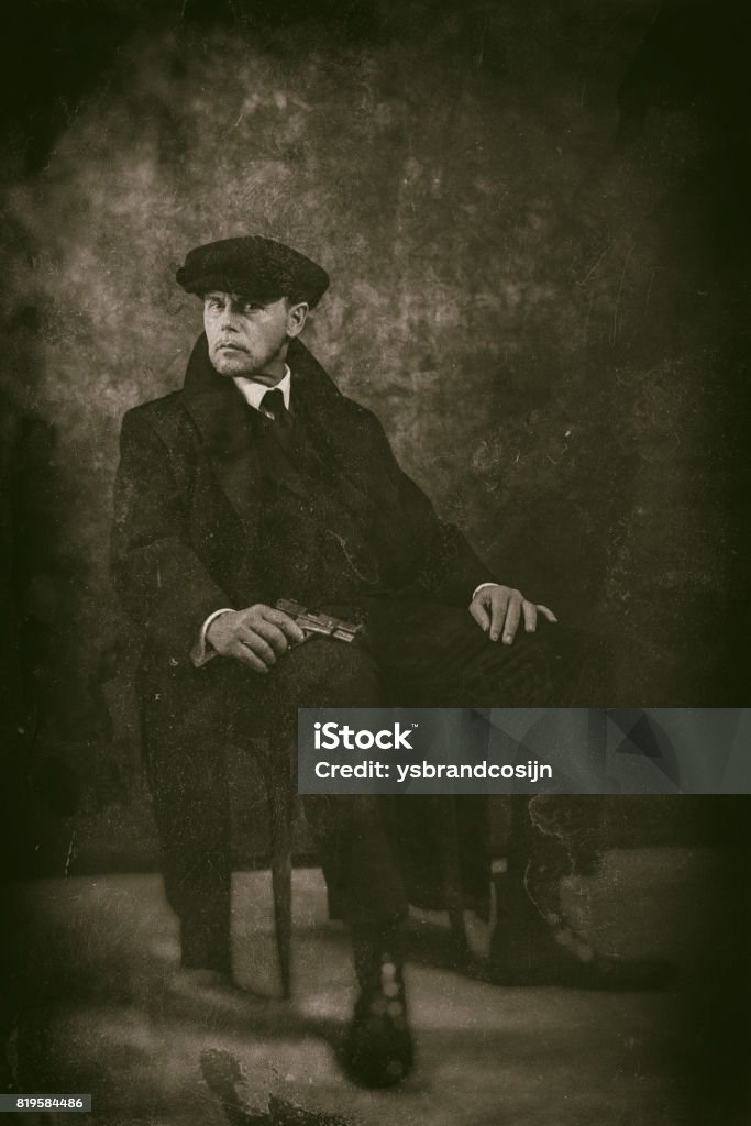 Retro 1920s english gangster with gun sitting on chair. Peaky blinders style. England Stock Photo