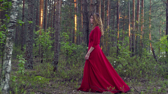 Young attractive woman in a long red dress walking in the forest