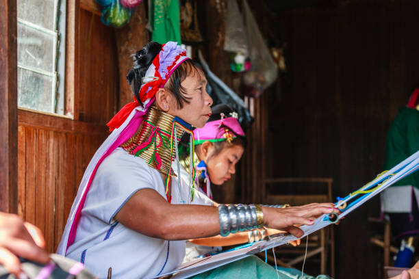 Unidentified Padaung senior woman wearing the traditional metal rings around her neck, INLE LAKE,MYANMAR-FEBRUARY 15,2016 : Unidentified Padaung senior woman wearing the traditional metal rings around her neck, working at a weaving in village of Inle lake, Shan state, Myanmar. unidentified padaung karen tribe woman weave on traditional device stock pictures, royalty-free photos & images