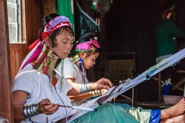 Unidentified Padaung senior woman wearing the traditional metal rings around her neck, INLE LAKE,MYANMAR-FEBRUARY 15,2016 : Unidentified Padaung senior woman wearing the traditional metal rings around her neck, working at a weaving in village of Inle lake, Shan state, Myanmar. unidentified padaung karen tribe woman weave on traditional device stock pictures, royalty-free photos & images