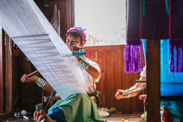 Unidentified Padaung senior woman wearing the traditional metal rings around her neck, INLE LAKE,MYANMAR-FEBRUARY 15,2016 : Unidentified Padaung senior woman wearing the traditional metal rings around her neck, working at a weaving in village of Inle lake, Shan state, Myanmar. unidentified padaung karen tribe woman weave on traditional device stock pictures, royalty-free photos & images