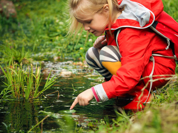 istock Child plays a puddle. Bright clothing - rubber boots and jacket. Summer, green grass 819620894