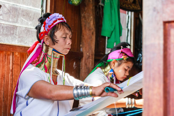 Unidentified Padaung senior woman wearing the traditional metal rings around her neck, INLE LAKE,MYANMAR-FEBRUARY 15,2016 : Unidentified Padaung senior woman wearing the traditional metal rings around her neck, working at a weaving in village of Inle lake, Shan state, Myanmar. unidentified padaung karen tribe woman weave on traditional device stock pictures, royalty-free photos & images